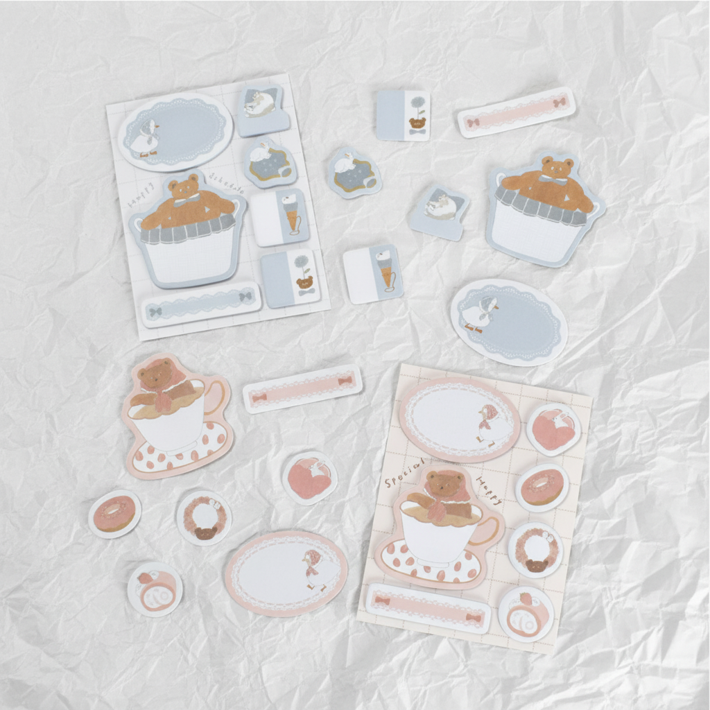 A set of cute, pastel-themed sticker sheets and individual stickers featuring a cupcake, coffee cup, and bunny motifs, arranged on a brown textured leather background.